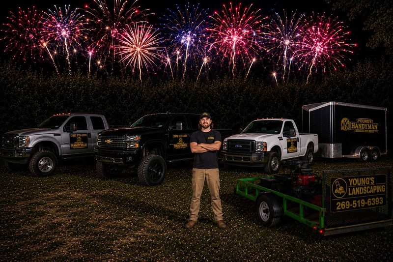 The Young's Handyman & Landscaping fleet with the owner out front and fireworks overhead